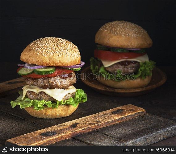 large burger with two fried cutlets, cheese and vegetables in a round wheat flour bun