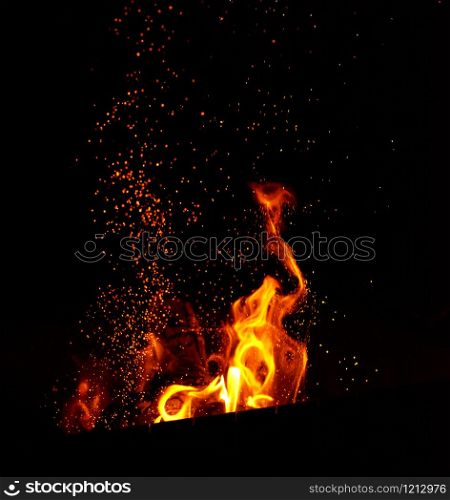 large burning bonfire with flame and orange sparks that fly in different directions on a black background