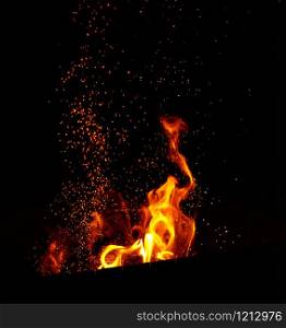 large burning bonfire with flame and orange sparks that fly in different directions on a black background