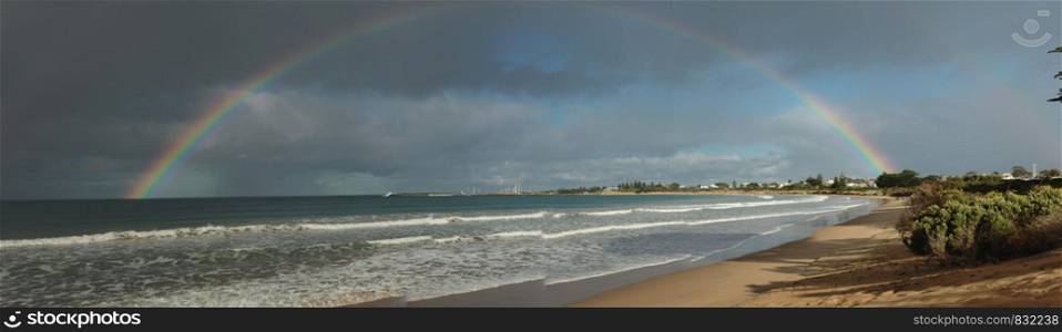 large complete full half circle rainbow stretching across the sky into the ocean at Apollo Bay, Victoria, Australia