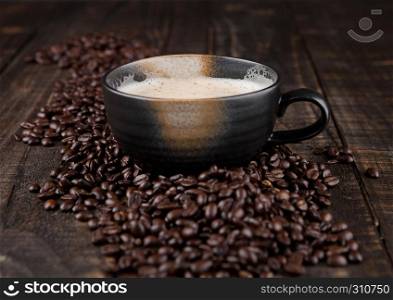 Large cup with hot cappuccino with coffee beans on wooden board