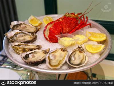 Large dish with fresh seafood, oysters with lobster with lemon and sauce on ice in a restaurant