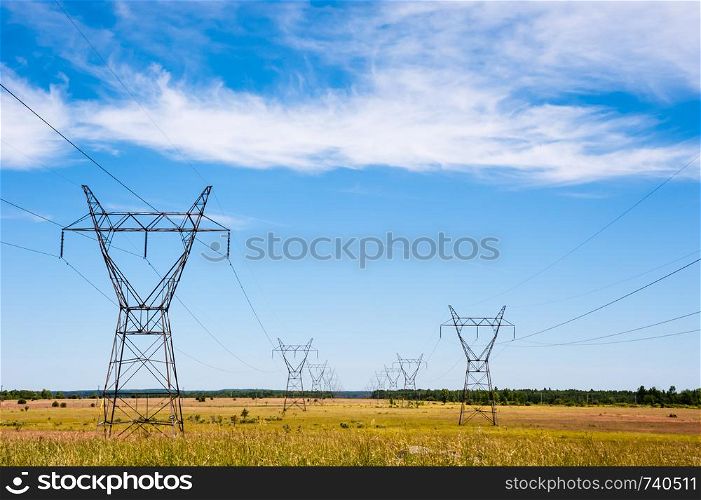 Large electrical transmission towers and power lines receding into distance on rural fields under partly cloudy sky.