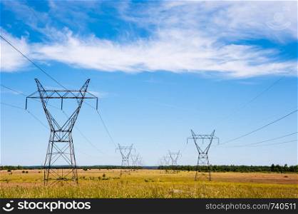 Large electrical transmission towers and power lines receding into distance on rural fields under partly cloudy sky.