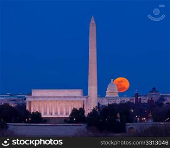 Large full moon rises through the haze over the Capitol building in Washington DC with Lincoln Memorial and Washington Monument aligned