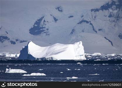 Large iceberg swims in a beautiful light mood in front of dark mountains covered with snow