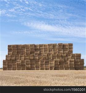 large piles of stacked straw bales in the noerth of france under blue summer sky