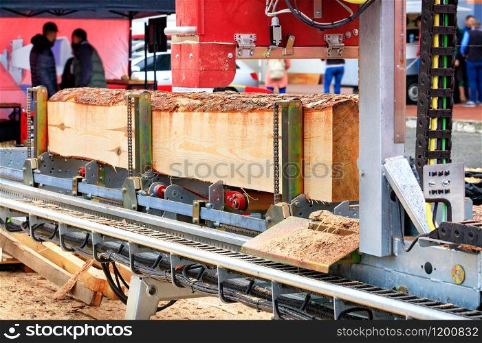 Large pine logs are processed at a modern automatic sawmill, receiving boards of a given size.. Modern woodworking machinery, processing of logs on an automatic sawing machine, close-up.