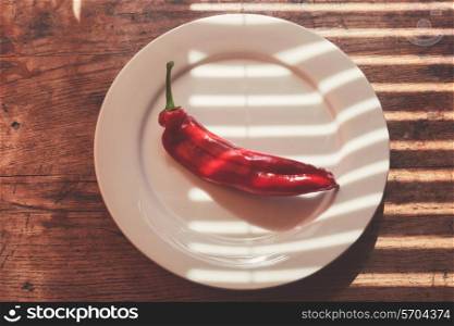 Large red pepper and a plate on a wood table in the sunlight