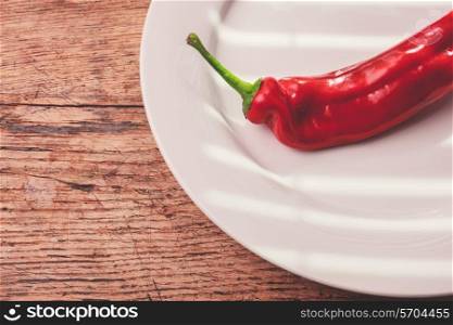 Large red pepper and a plate on a wood table in the sunlight