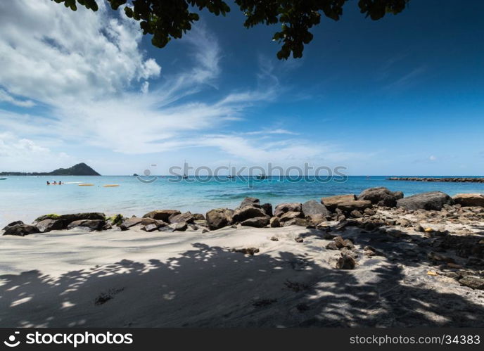 Large rocks and shadows on the beach in front of the sea with boats, in Saint Lucia