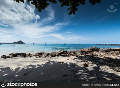 Large rocks and shadows on the beach in front of the sea with boats, in Saint Lucia
