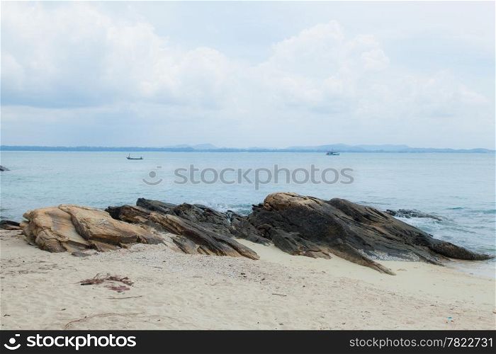 Large rocks on a sandy beach with small fishing boats in the sea.