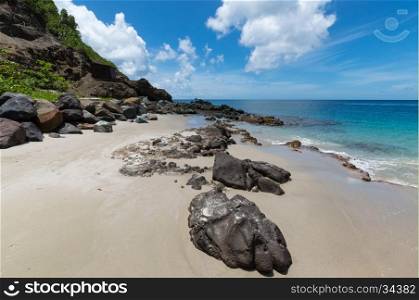 Large rocks on the sand and at the side of a hill with the sea beyond