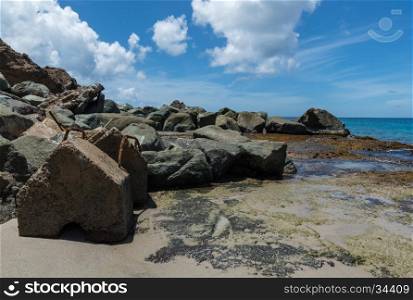 Large rocks, some with rusty iron bars, on the sand with the sea in the background, in Saint Lucia