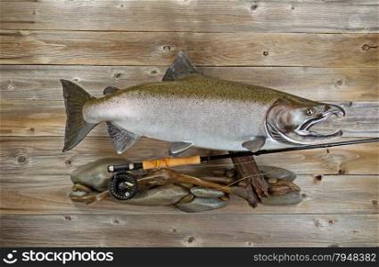 Large salmon with fly rod and reel on rocks and rustic wood.