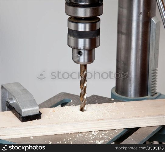 Large sized drill in solid chuck drilling deep into wood and throwing shavings about the surface