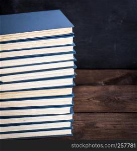 large stack of books in a blue cover on a brown wooden table, copy space