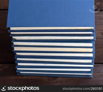 large stack of books in a blue cover on a brown wooden table, top view
