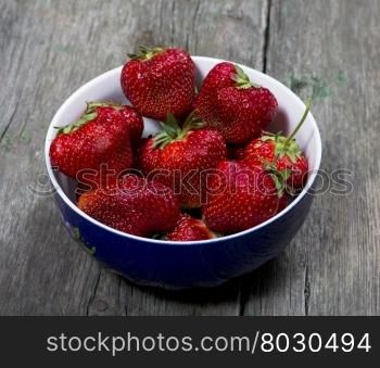large strawberries in a blue plate, on a wooden table, a berry subject
