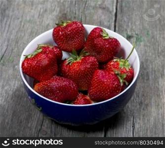 large strawberries in a blue plate, on a wooden table, a berry subject