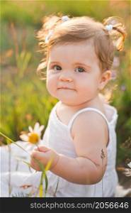 Large sunny portrait of a child with a daisy flower.. The child is smiling happily while sitting in the field 3017.