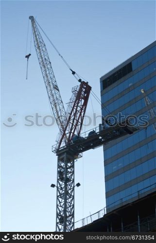 Large tall building crane next to building against bright blue sky with copy space.
