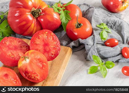 Large variety of tomatoes on rustic kitchen counter. Preparation of tomato sauce with onions and basil