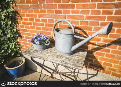 Large water can in metal on a wooden stand in a backyard with flowers and plants
