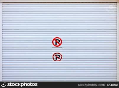Large white metal shutters, garage doors with an inscribed sticker do not park at the entrance to the car parking. Texture and background closeup, image with copy space.. Large white metal shutters at the entrance to the car parking.