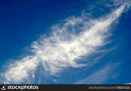 Large wispy cirrus cloud in diagonal feather shape on azure blue sky background.