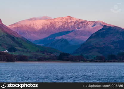 Last sun of the day on snow covered Snowdon Mountain. Landscape with Nantlle Lake in foreground.