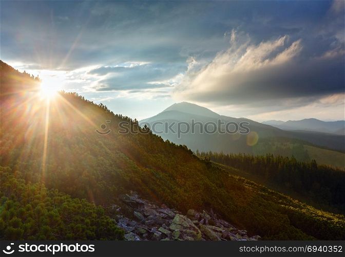Last sun rays in evening sky with clouds above Syniak mountain. Summer sunset view from Homiak mountain, Gorgany, Carpathian, Ukraine. Some sun flare effect available.