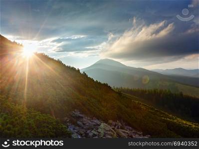 Last sun rays in evening sky with clouds above Syniak mountain. Summer sunset view from Homiak mountain, Gorgany, Carpathian, Ukraine. Some sun flare effect available.