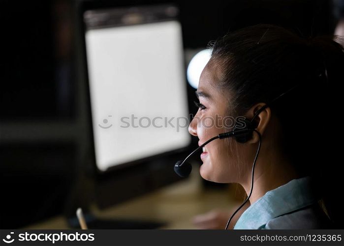 Late Night Environment. Side view young adult friendly Call centre operator with headsets working hard at night. Using for 24 Hr. 7 days Call center Concept.