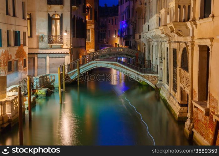 Lateral canal and pedestrian bridge in Venice at night with street light illuminating bridge and houses, Italy