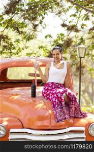 Latin brunette woman next to a bottle of wine on a classic car