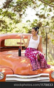 Latin brunette woman next to a bottle of wine on a classic car