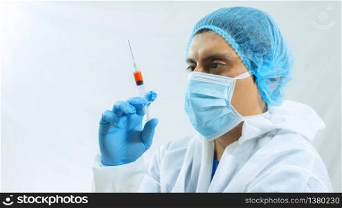 Latin doctor in bioprotective suit, face mask and blue gloves holding a syringe with a blood sample staring at her with eyes on white background. Latin doctor in bioprotective suit, face mask and blue gloves holding a syringe with a blood sample on white background