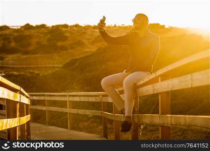 Latin man taking selfies with a smartphone over an amazing sunset landscape view. Natural outdoor light