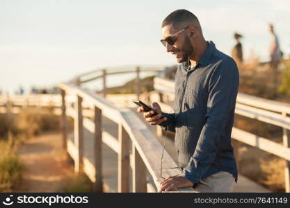 Latin man texting with a smartphone over an amazing sunset landscape view. Natural outdoor light