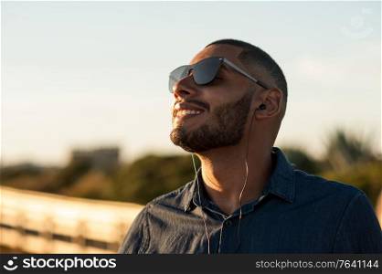 Latin man using earphones to listen music or motivational podcasts and enjoying the sunset. Natural warm light.
