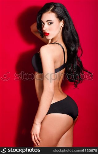 Latin woman wearing black bra and panties on red background. Studio shot.