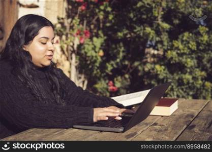 latin woman with long dark hair, typing on her laptop, working on a university educational project, outside in the park on the university c&us.. latin woman with long dark hair, working outdoors with laptop