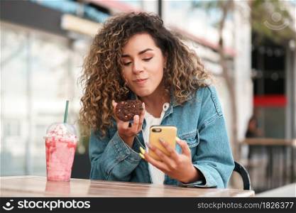 Latin young woman using her mobile phone while sitting at a coffee shop outdoors on the street. Urban concept.