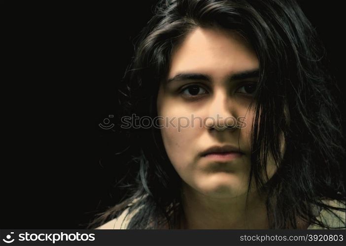 Latina teen in front of a black background and looking at the camera with a serious expression on her face.. Latina teen in front of black background looking at camera