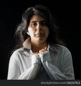 Latina teen in white long sleeved shirt standing in front of black backdrop. Latina teen in white on black backdrop