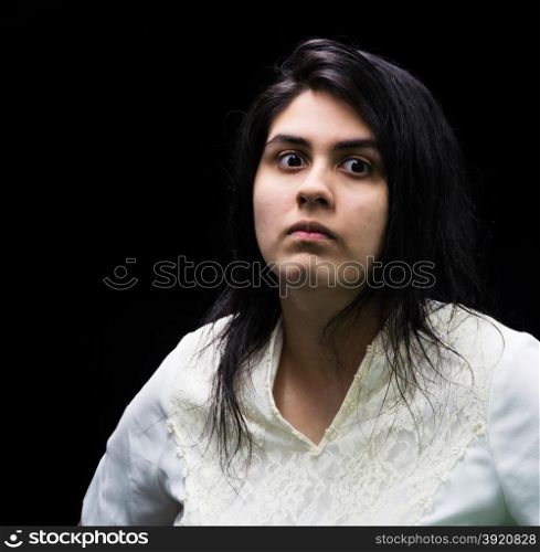 Latina teenager in white standing in front of a black background with an angry, suspicious, serious look on her face.