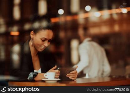 Latina woman in a coffee shop viewed through glass with reflections as they sit at a table chatting and laughing. woman in a coffee shop drink coffee viewed through glass with reflections as they sit at a table chatting and laughing