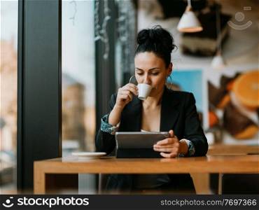 Latina woman sitting in cafe using tablet and drinks coffee on break from work. Latina woman sitting in a cafe on a break from work